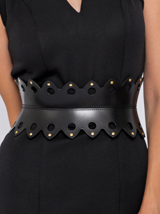 Close view of black leather hourglass belt being worn over black dress.