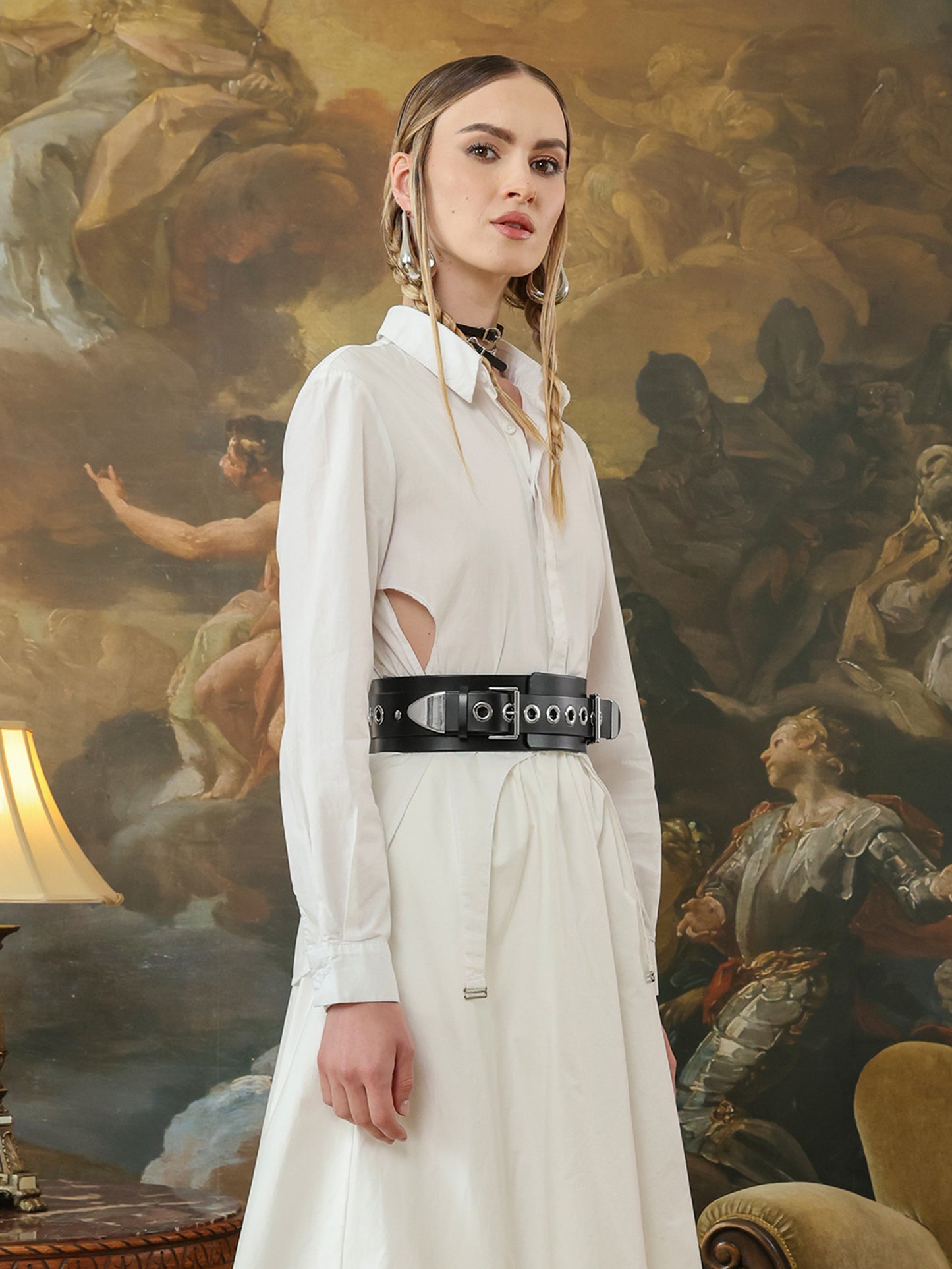 Woman wearing a black leather belt with silver grommets styled over a white dress.