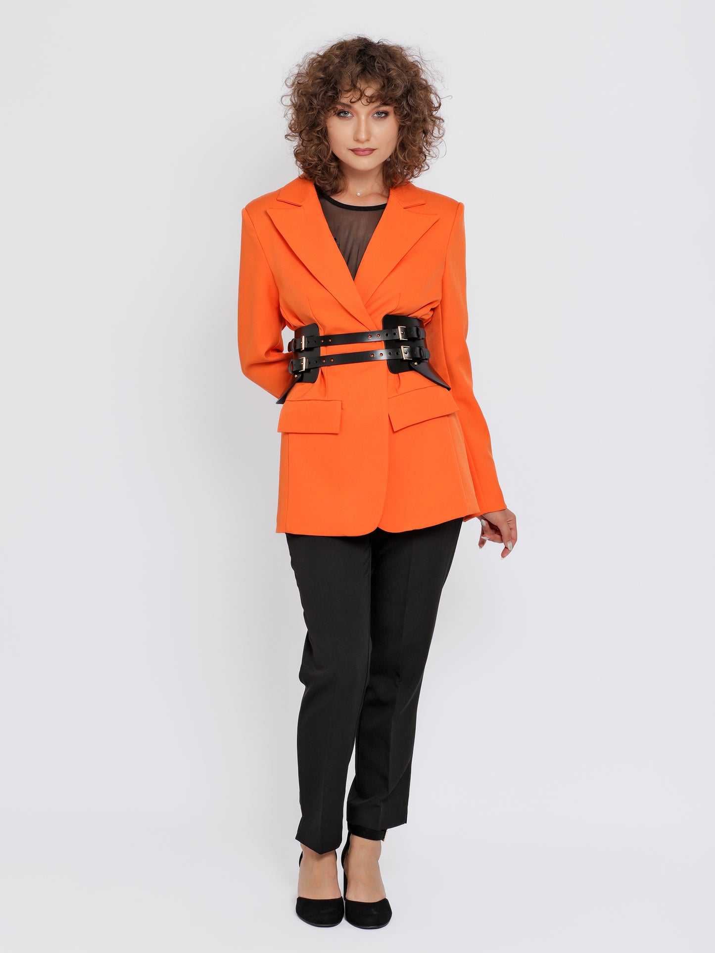 Full outfit view of black leather peplum belt being worn over orange blazer and black trousers.
