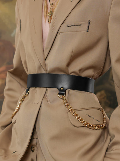 Woman wearing a black leather waist belt with gold chain details over a beige suit.