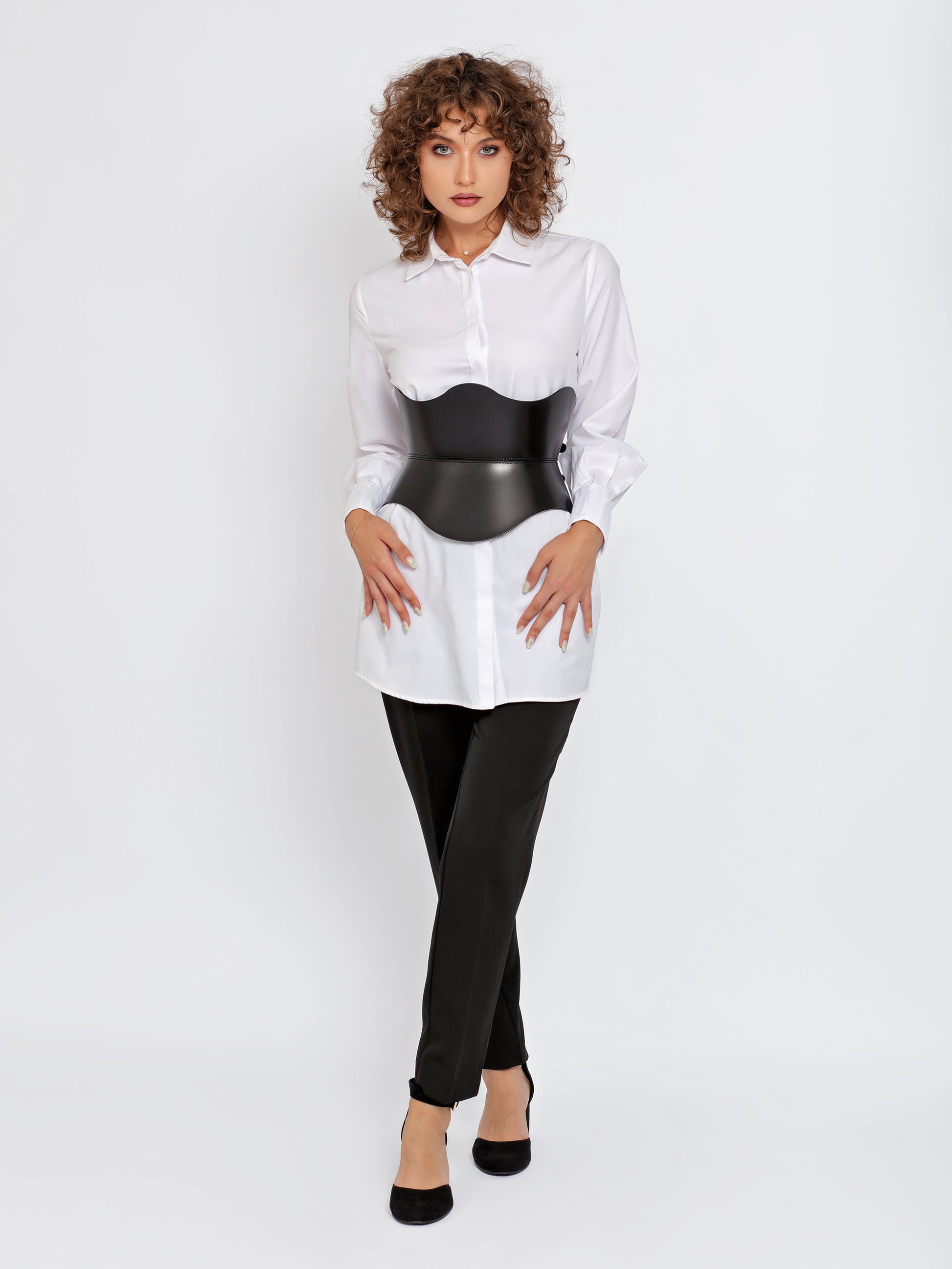 Full outfit view black corset belt worn over white shirt by model.