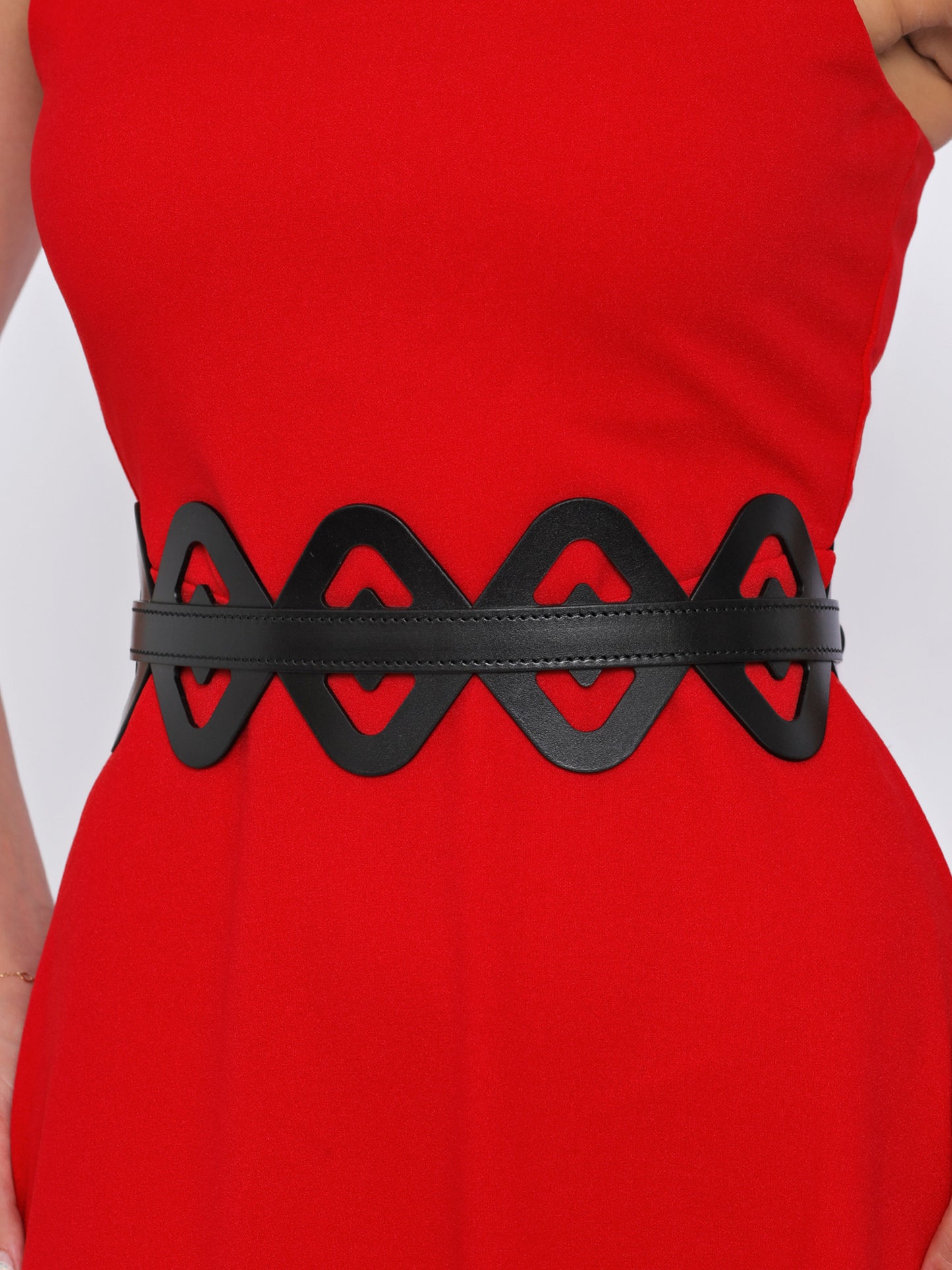 Close view of black wide leather belt being worn over red dress.