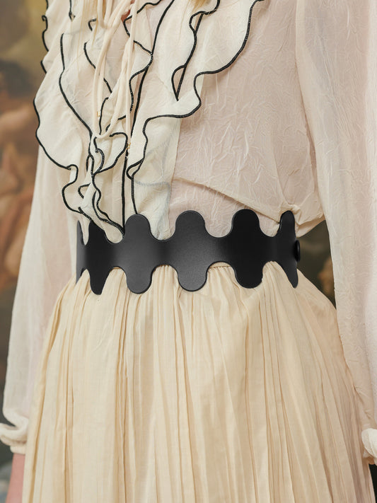 Close-up of a black leather high-waist belt with a wavy edge design paired with a cream pleated skirt and ruffled blouse.