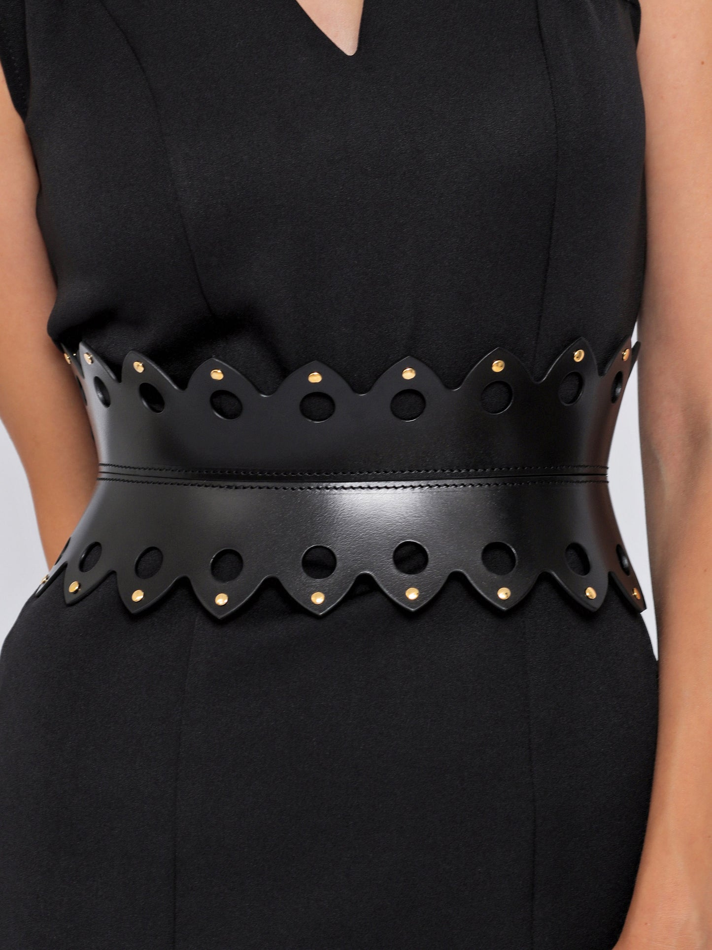 Close view of black leather hourglass belt being worn over black dress.