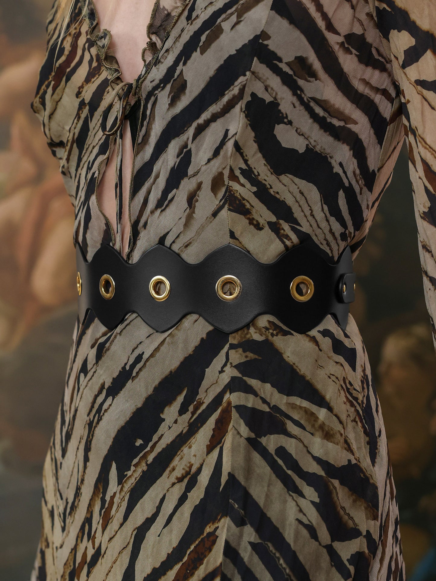 Black leather belt with eyelets styled over a printed dress – side view.