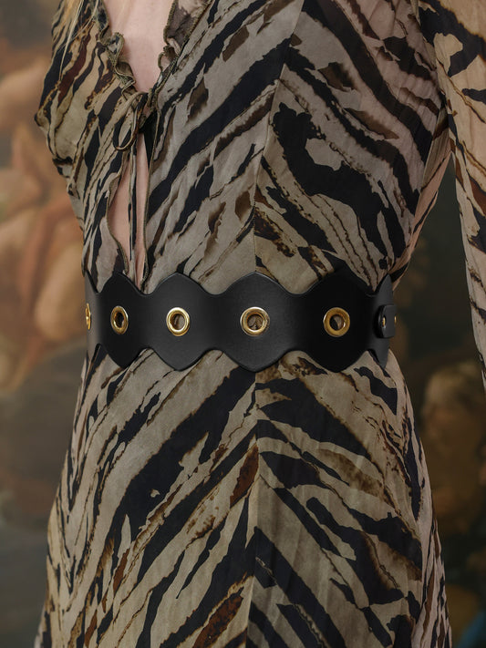 Black leather belt with eyelets styled over a printed dress – side view.