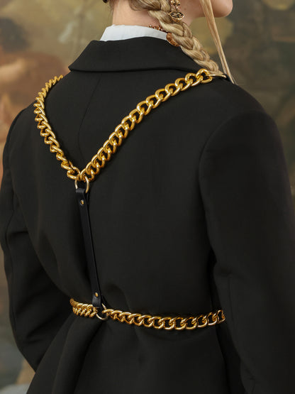 Close-up of black leather harness with bold gold chain straps across the back of a black blazer.