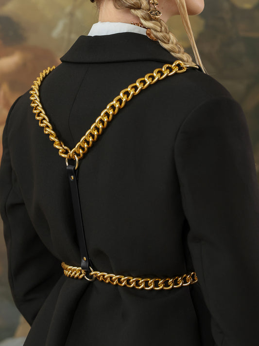 Close-up of black leather harness with bold gold chain straps across the back of a black blazer.