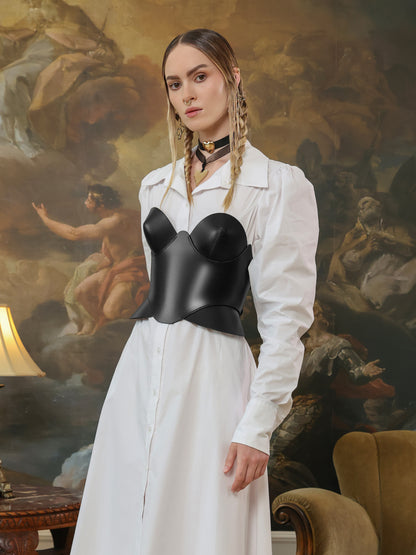 Black leather overbust corset top styled over a white button-down midi dress.