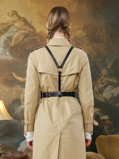 Back view of a beige trench coat styled with a black leather harness belt featuring gold-tone ring and buckle details.