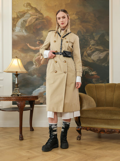 Full-length look with a beige trench coat paired with a black leather harness belt and attached micro bag.