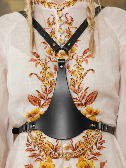 Close-up of black leather waist harness with chains and gold ring detail.