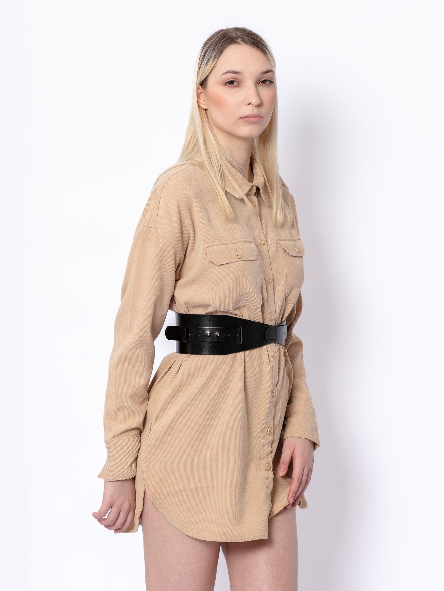 Side view of black leather corset belt worn by model over beige shirt.