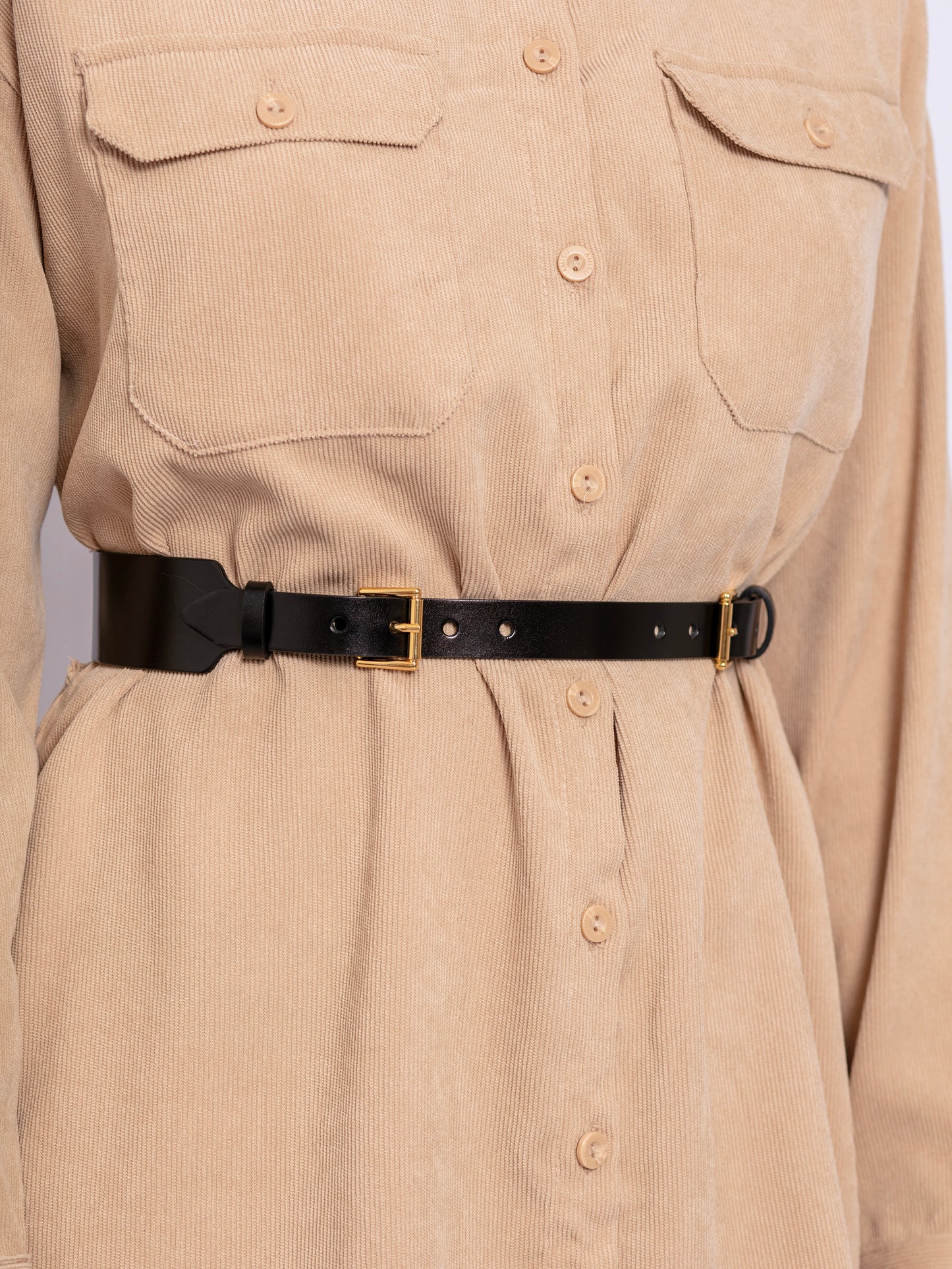 Detailed view of black leather belt worn over beige shirt.