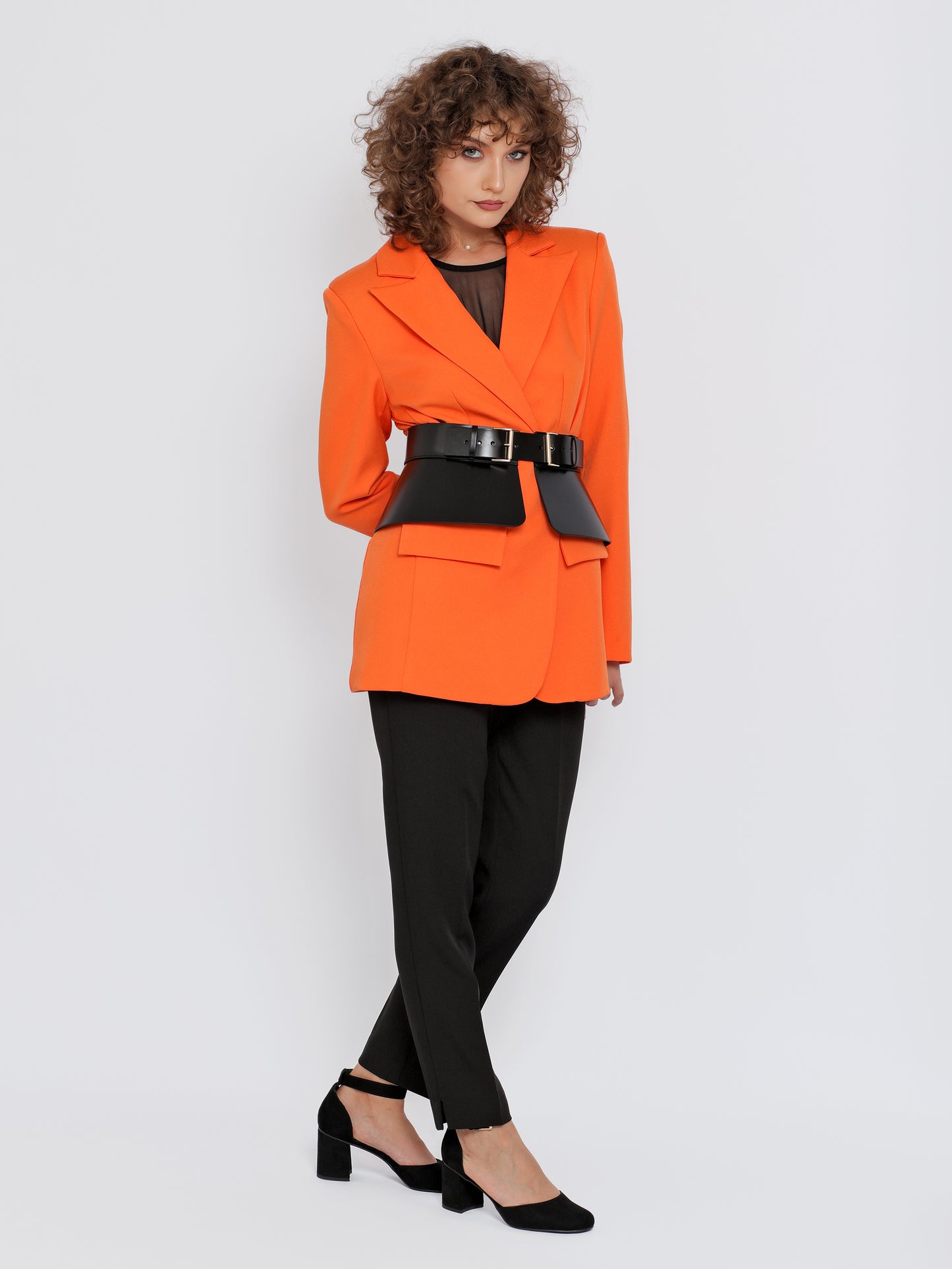 Full outfit view of black peplum leather belt being worn over orange blazer.