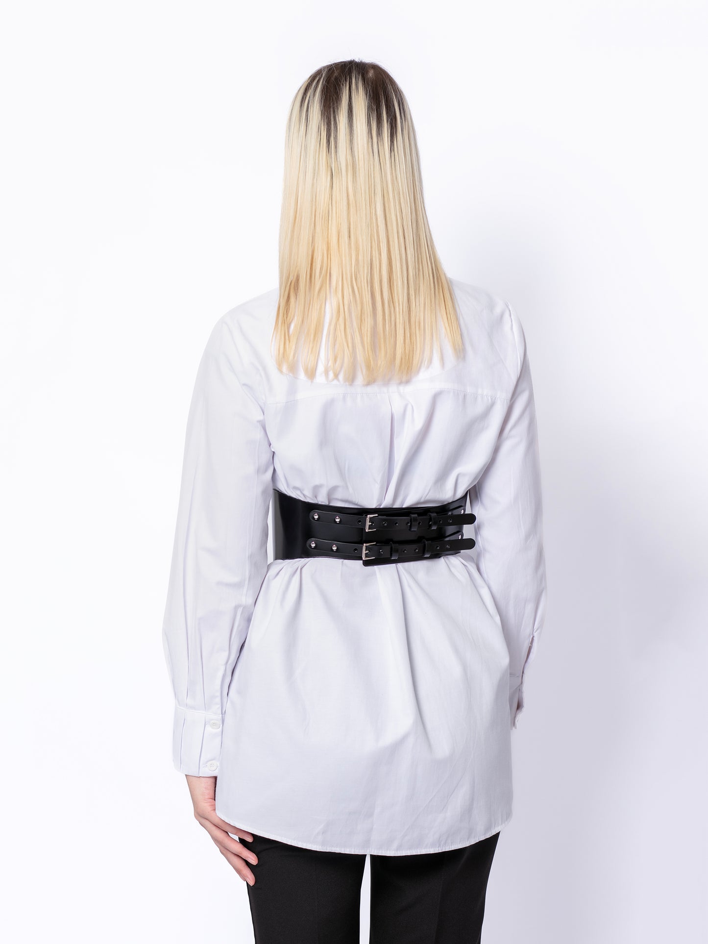 Back view of corset leather belt worn by woman over white shirt.