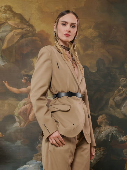 Front view of a woman wearing a tailored beige suit with a black waist belt featuring angular cutouts.