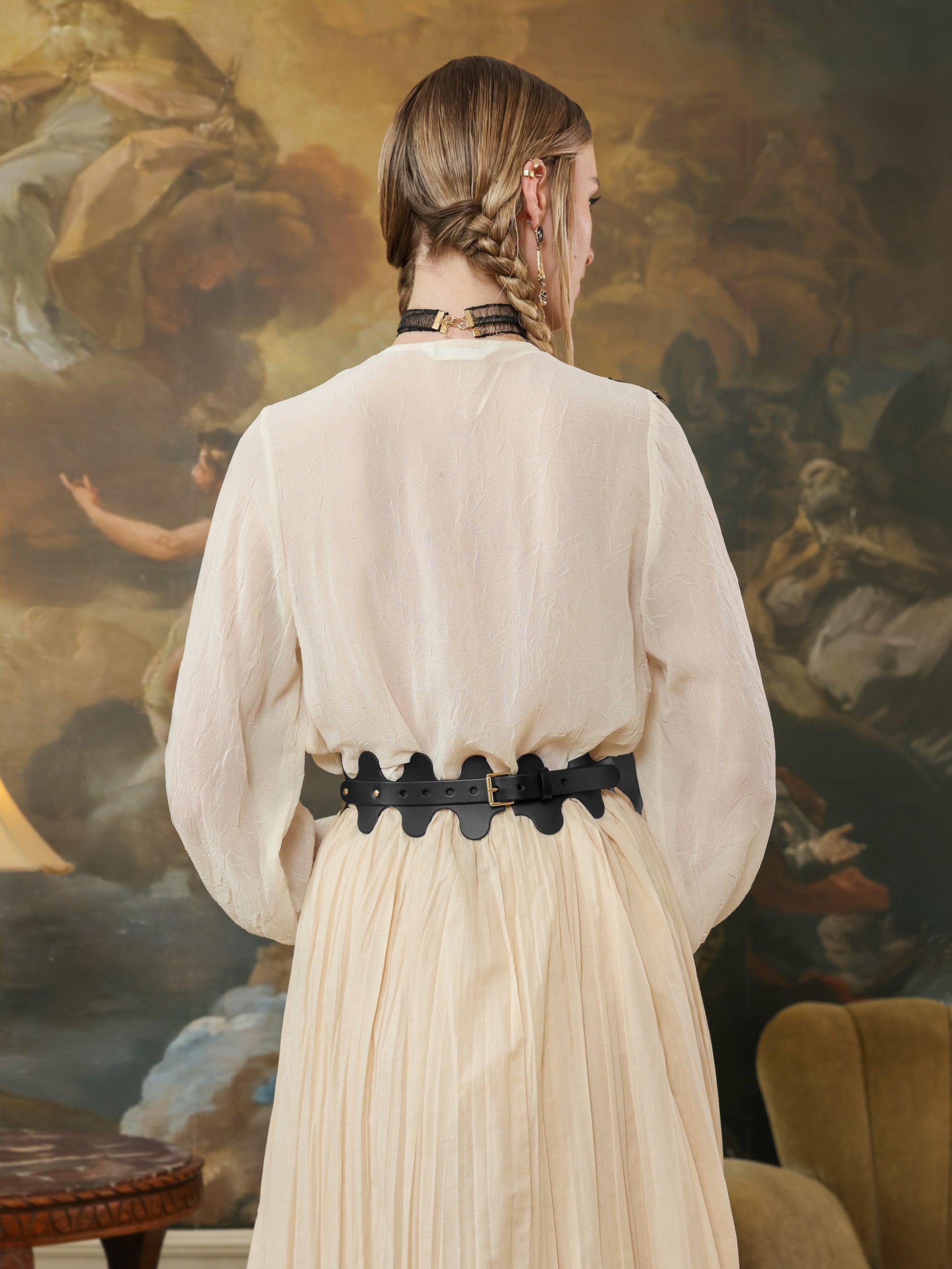 Back view of a black leather high-waist belt with wave design, secured with a buckle, styled with a flowy cream skirt.
