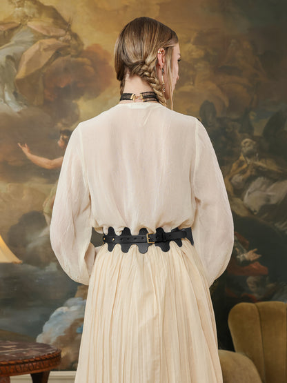 Back view of a black leather high-waist belt with wave design, secured with a buckle, styled with a flowy cream skirt.