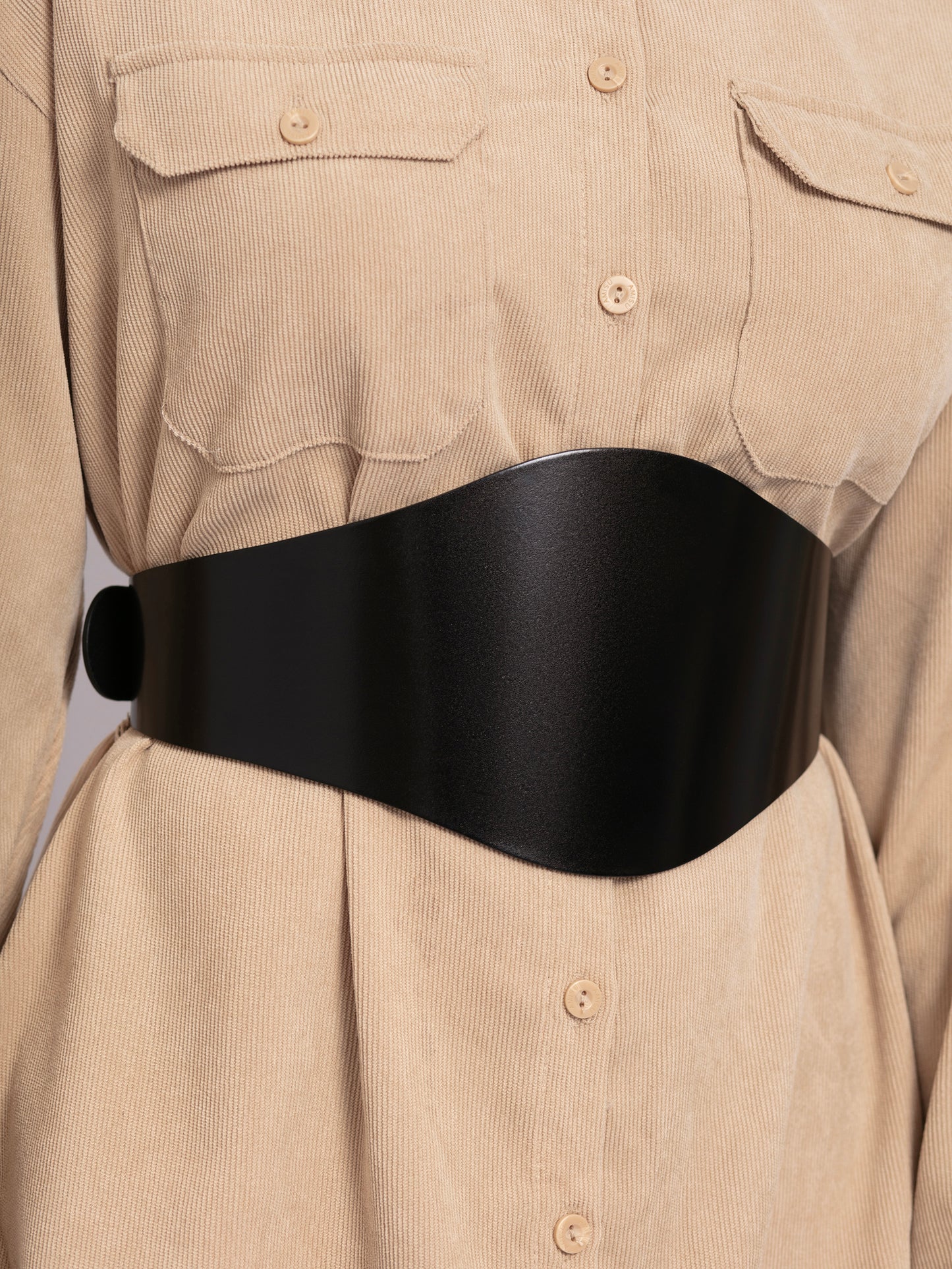 Close view of black wide leather belt worn over beige shirt.