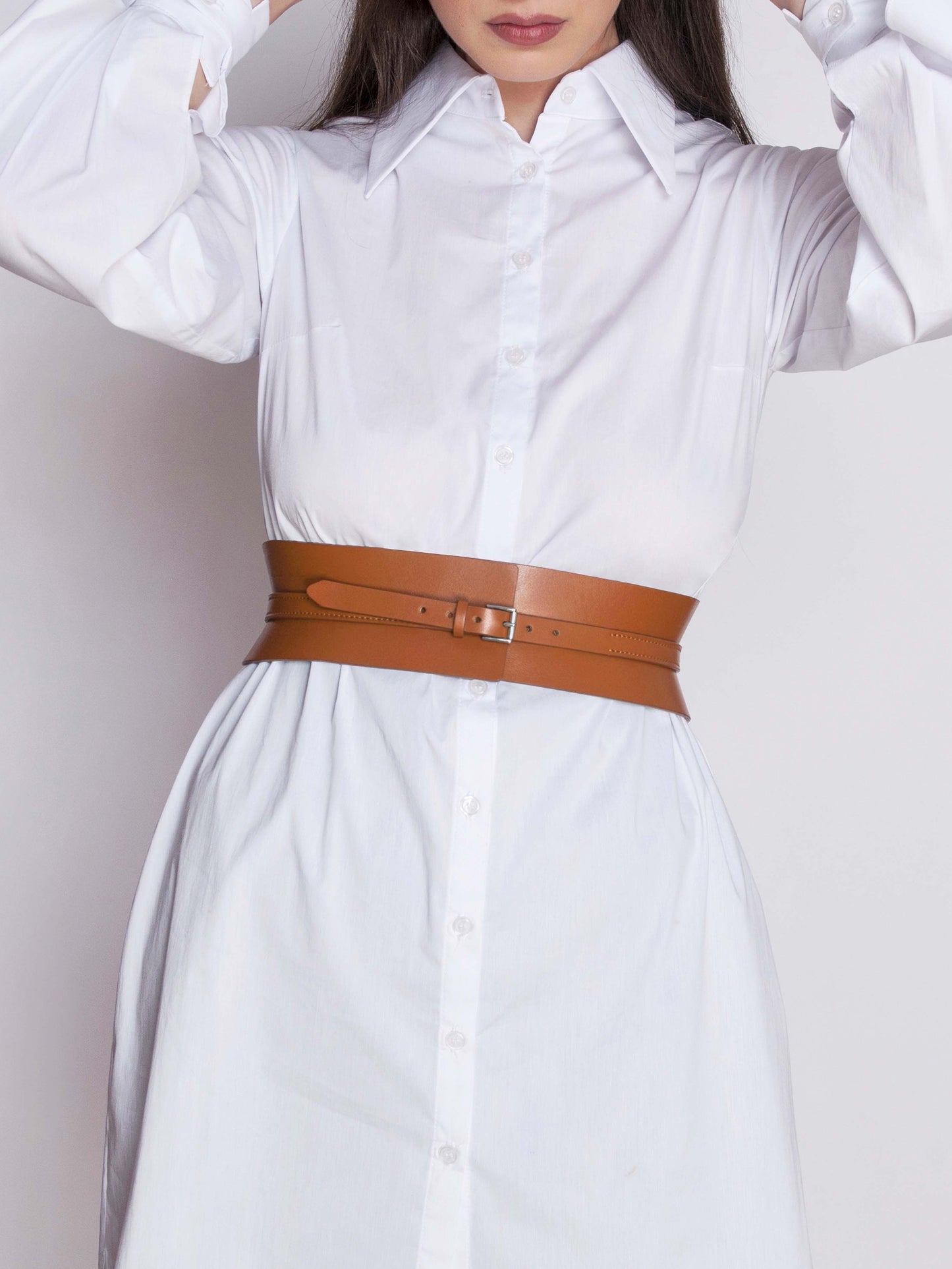 Brown leather corset belt fitted on woman wearing white shirt dress.