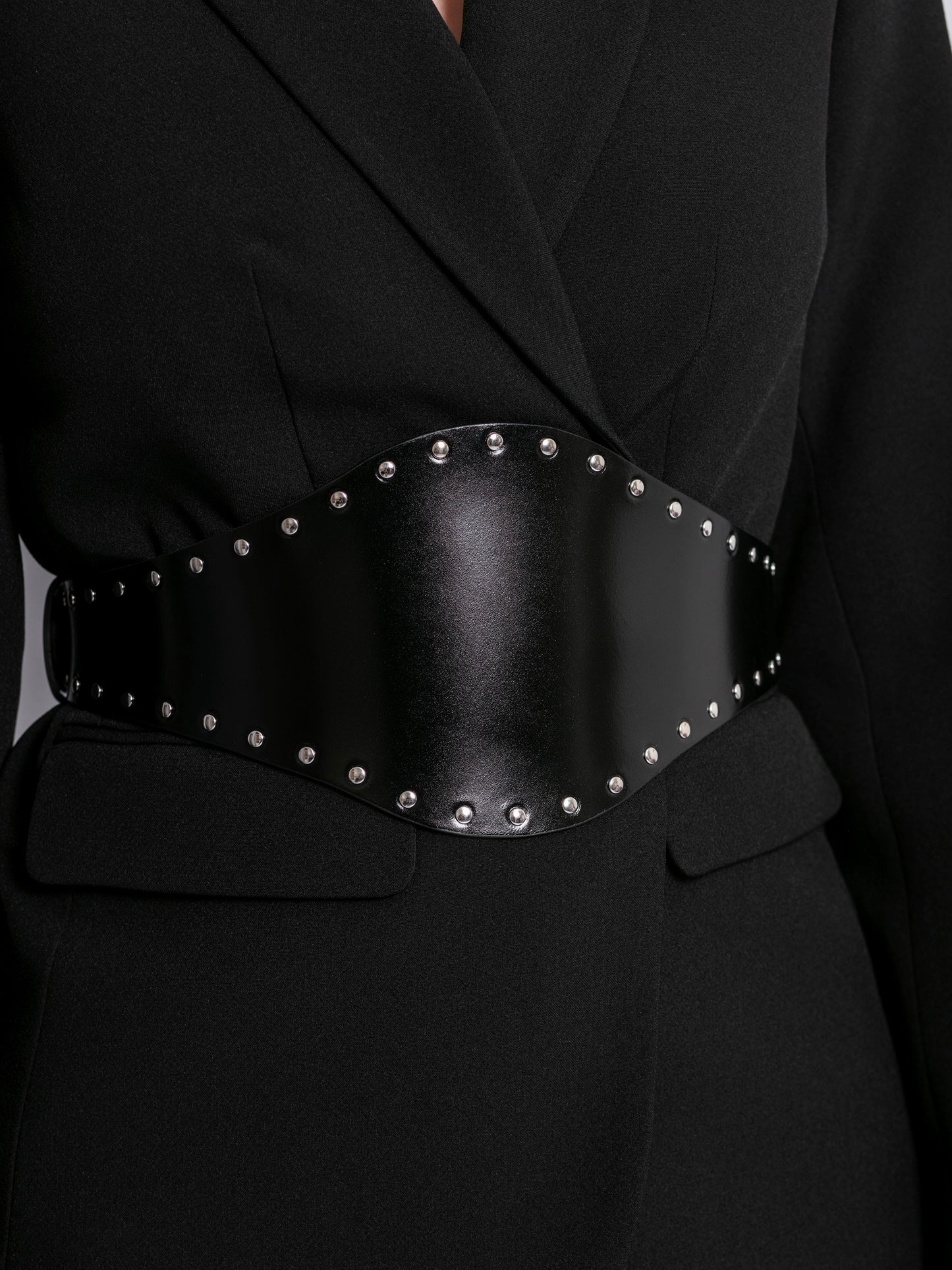 Close view of black wide belt worn over black blazer.