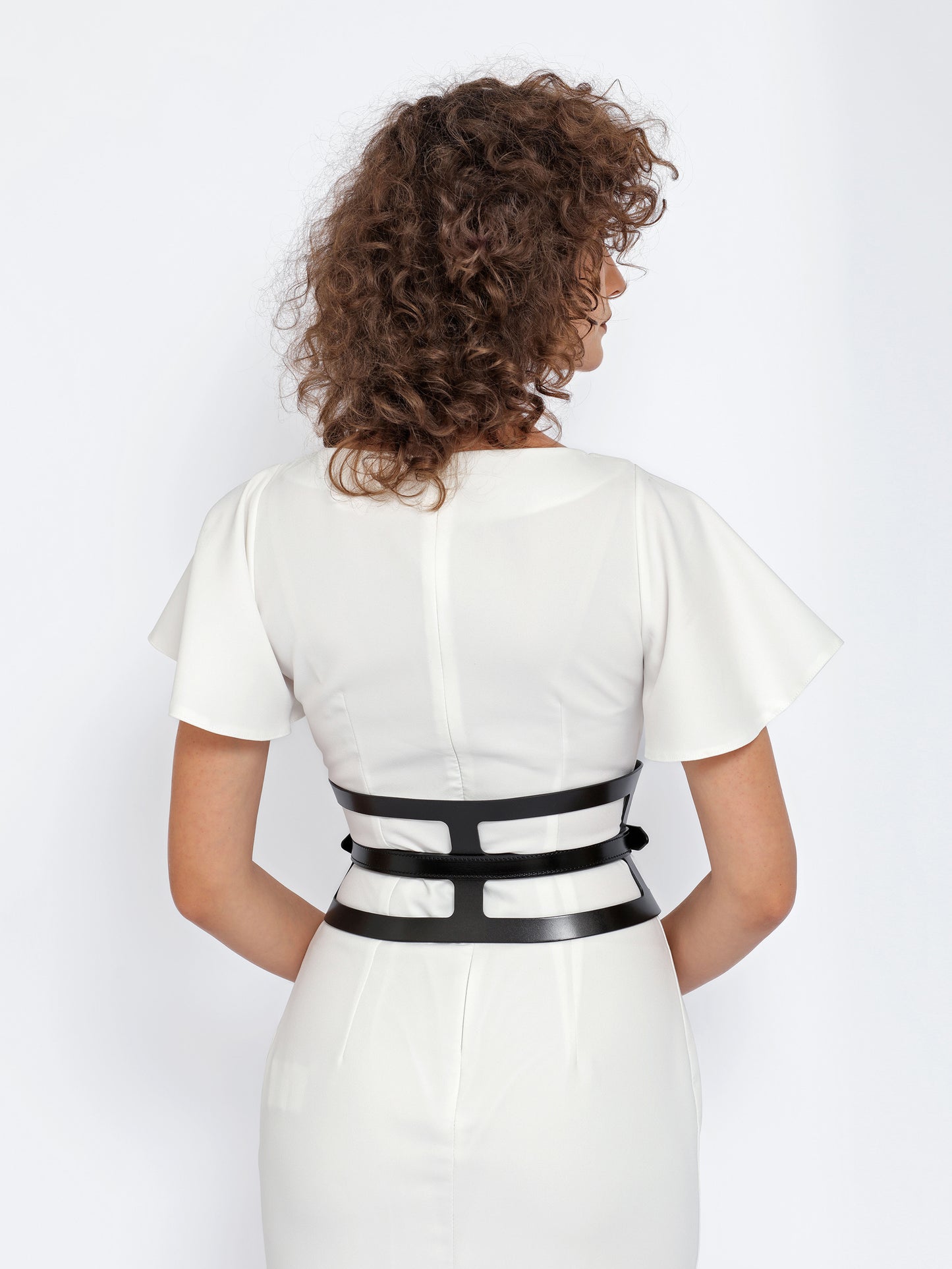 Back view of black leather corset belt being worn over white dress.