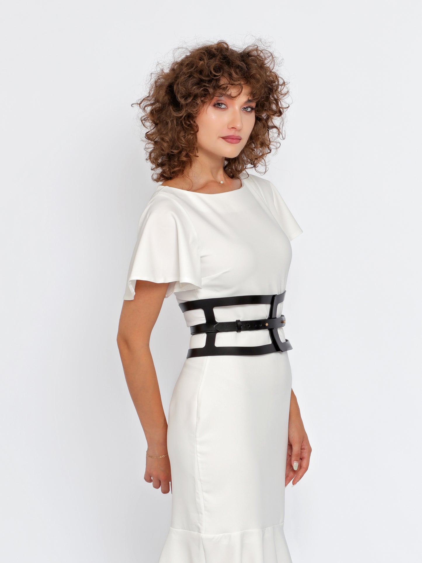 Side view of black leather hourglass belt being worn over white dress.