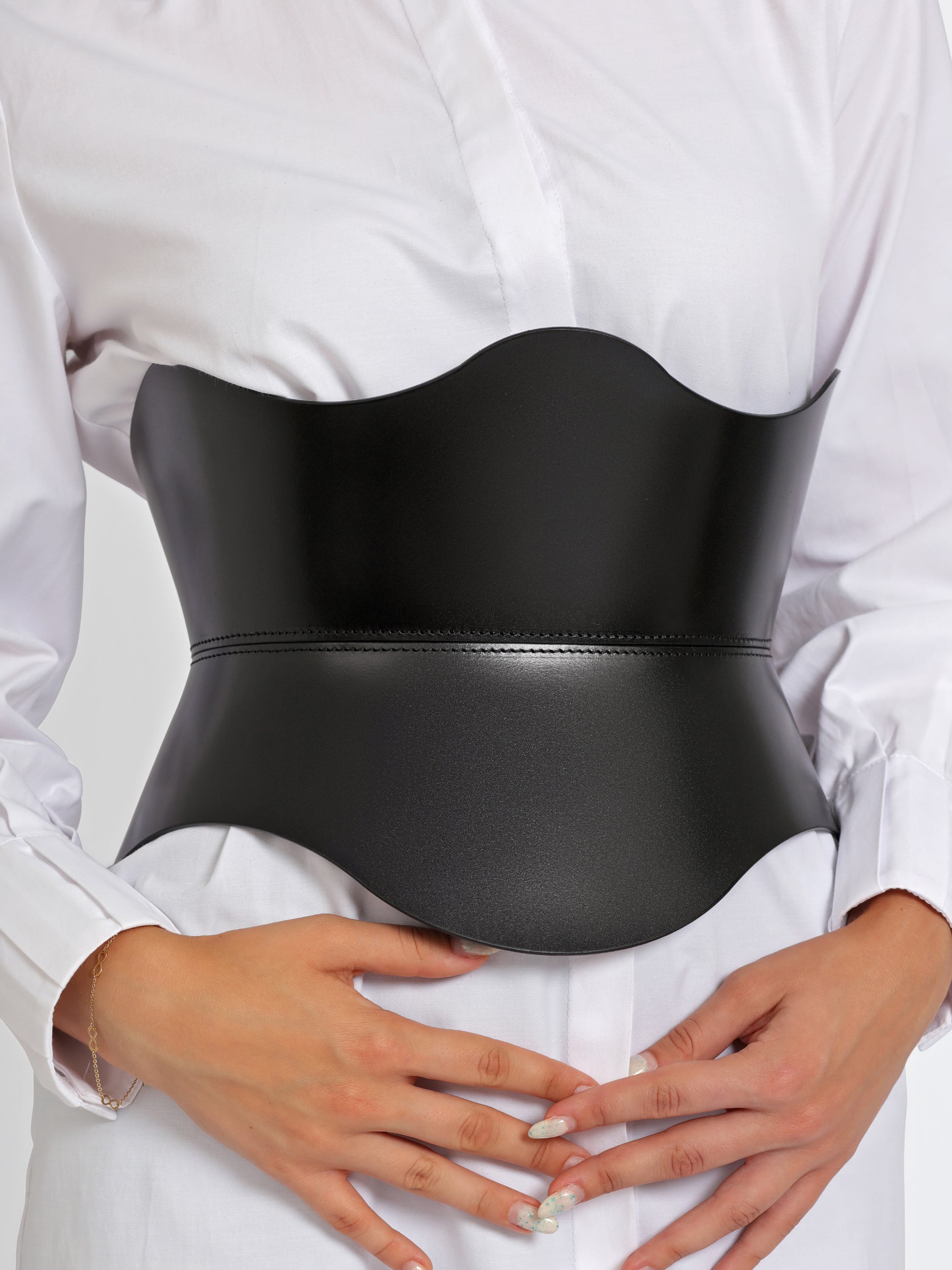 Close up view of black leather wide belt worn over white shirt by model.