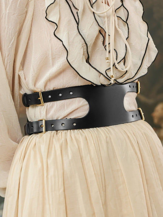 Person wearing a black belt with a gold buckle on a beige outfit.