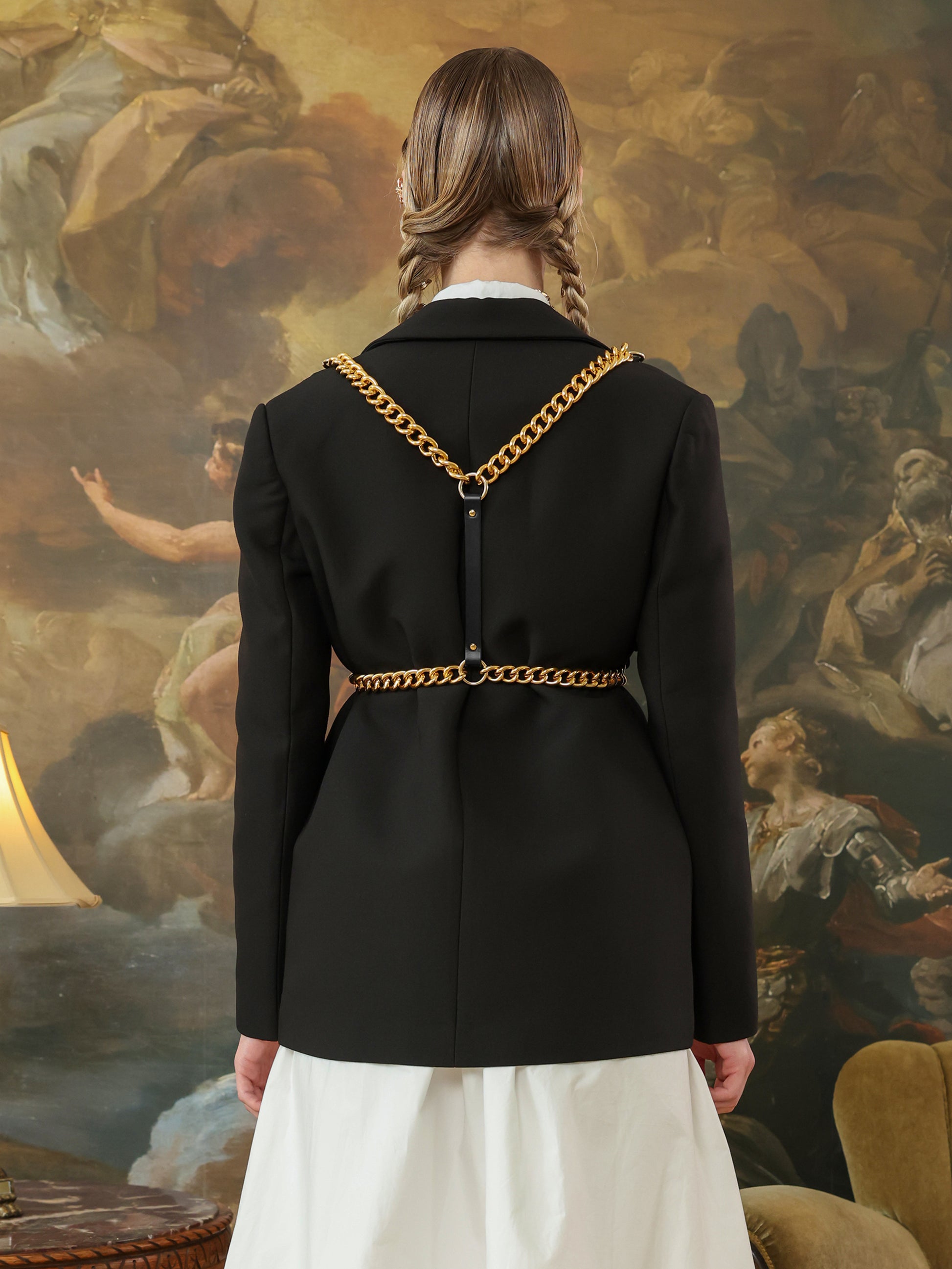 Back view of a black leather harness featuring gold chain details over a black blazer.