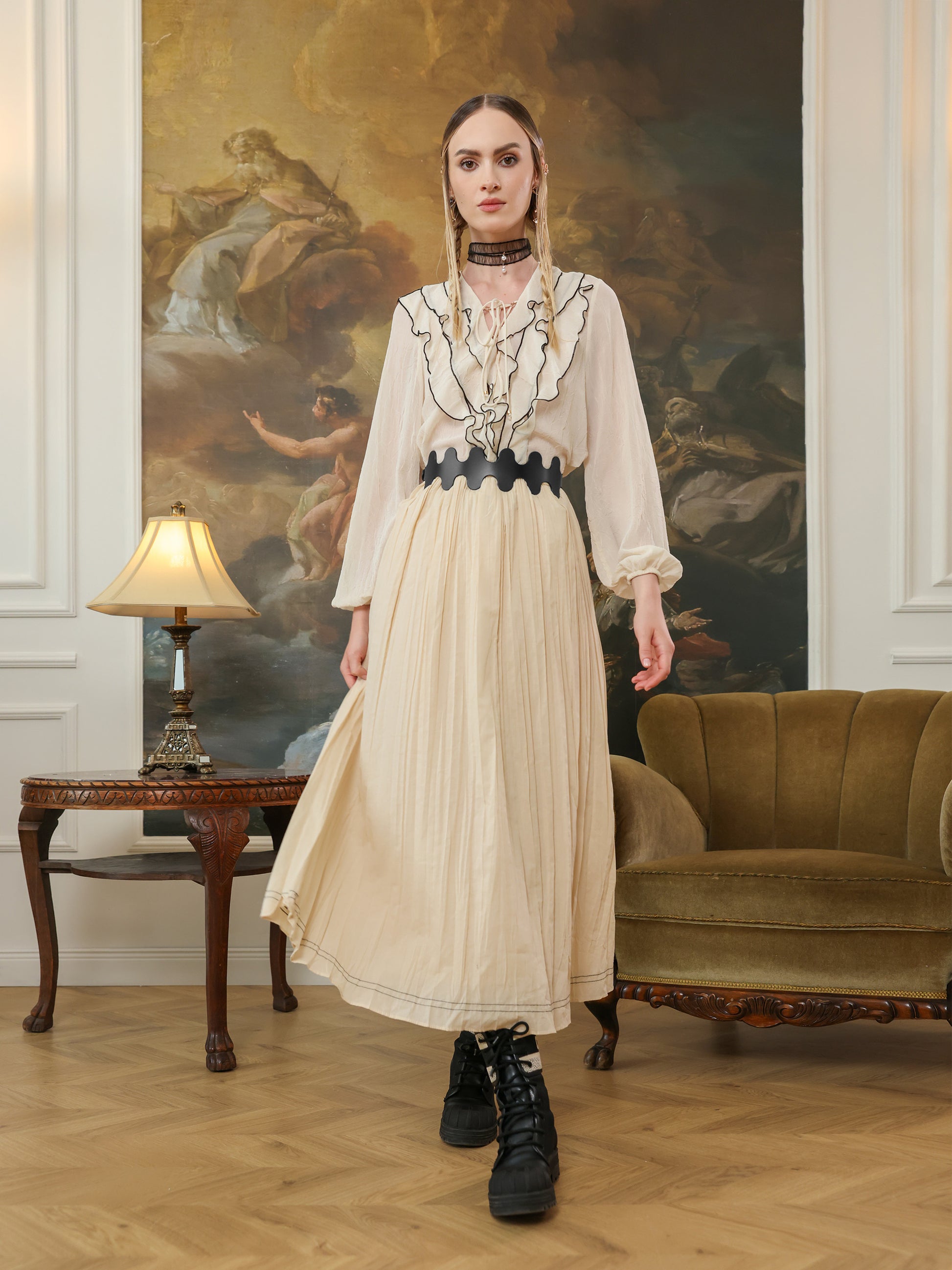 Full outfit featuring a cream ruffled blouse and pleated skirt styled with a black wavy high-waist belt and lace-up boots.