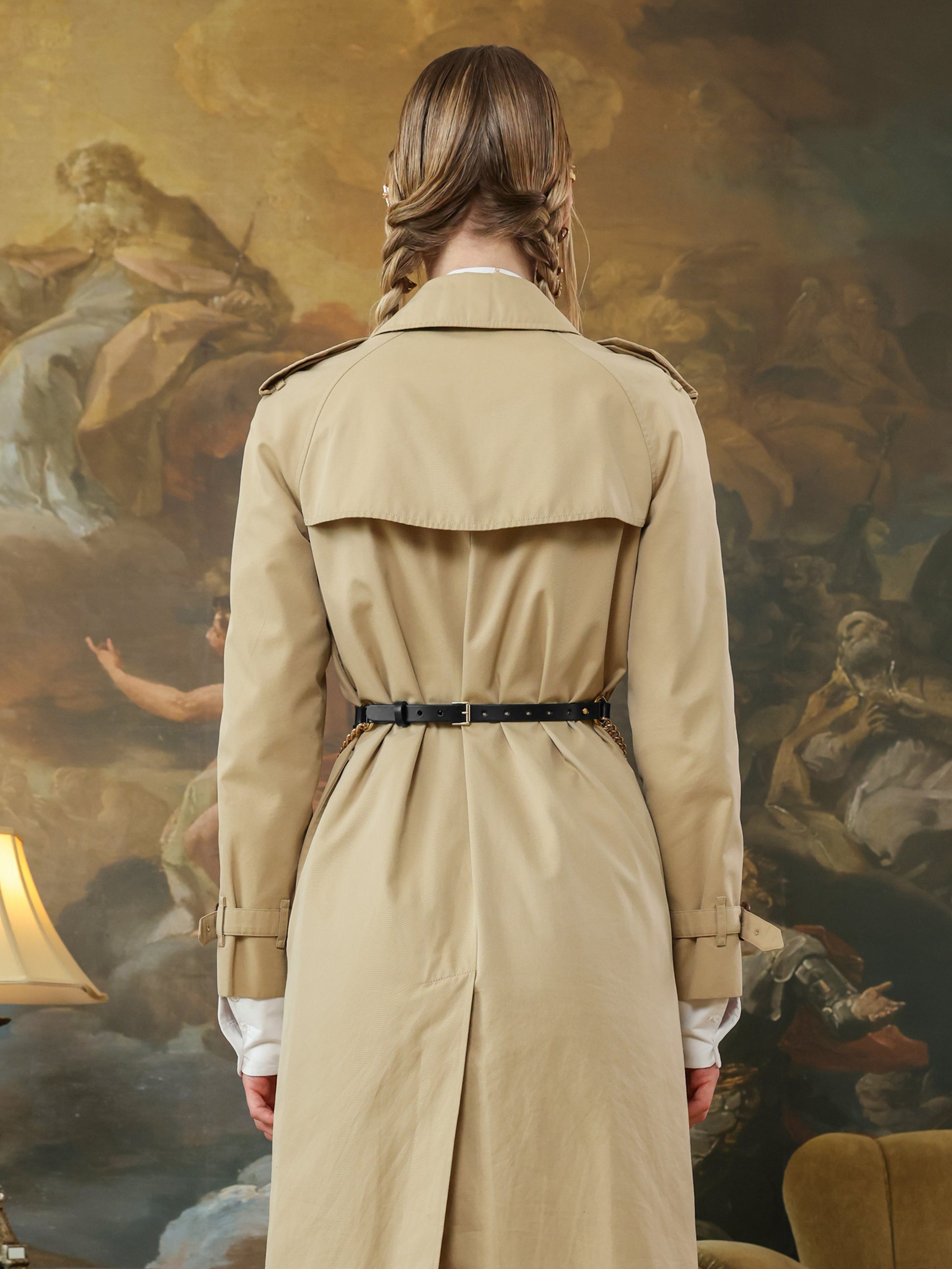 Back view of a beige trench coat with a wide black leather belt and adjustable buckle closure.