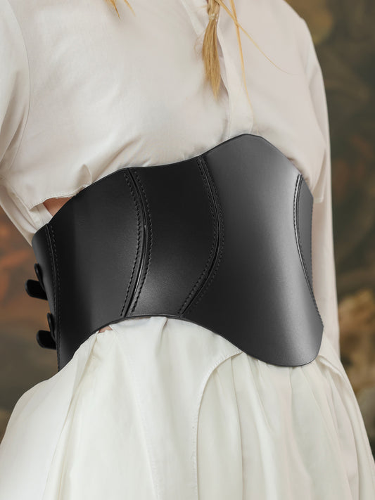 Side view of a wide black leather corset belt with curved seams, styled over a white outfit for a modern statement.