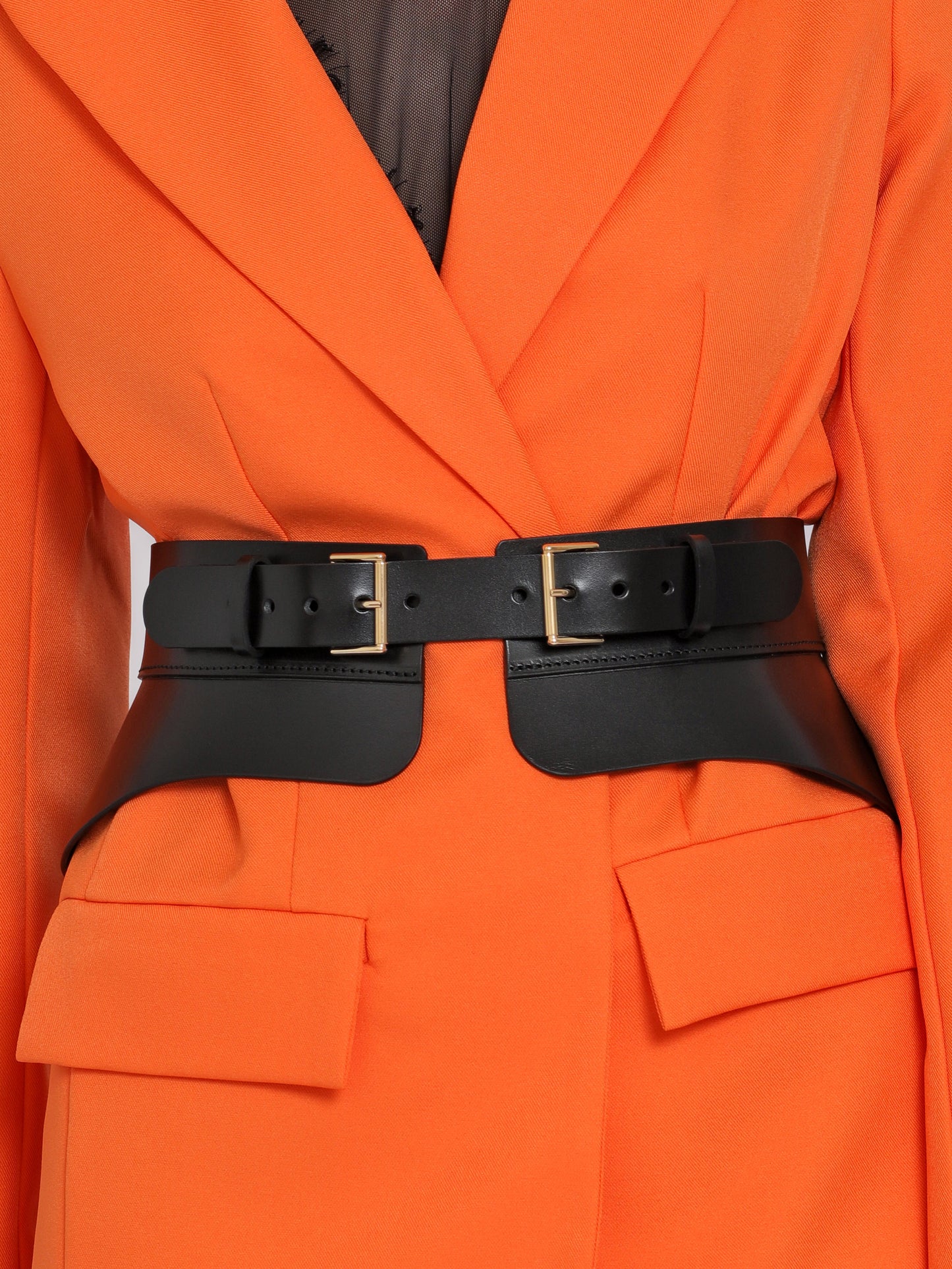 Close view of black leather peplum belt being worn over orange blazer.