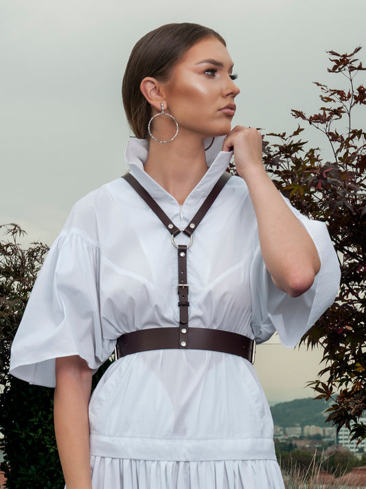 Leather body harness fittted on woman wearing white  shirt dress.