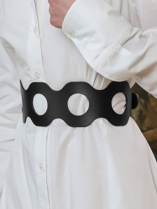 Statement black leather waist belt with circle cutouts, paired with a white long dress.