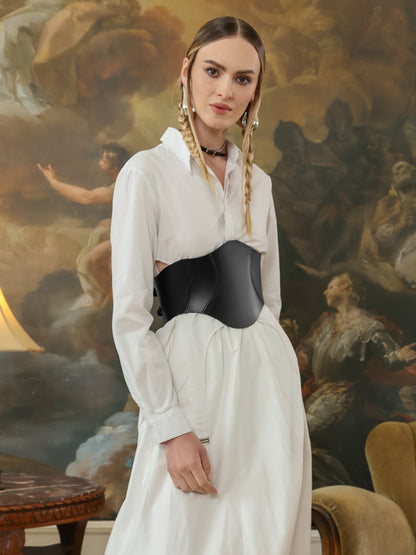 Model poses in a black leather corset belt layered over a crisp white dress, combining elegance with bold edge.