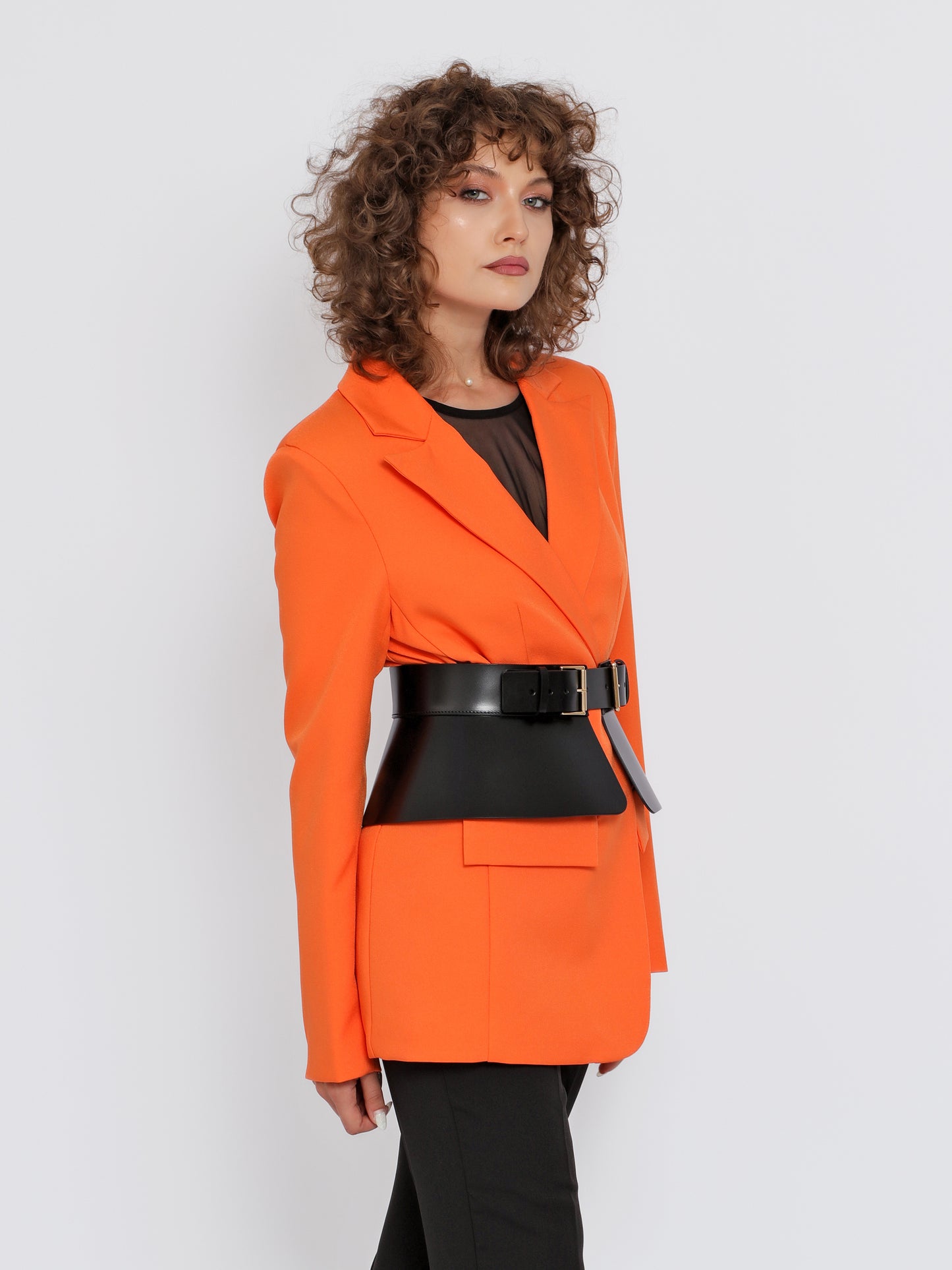 Side view of black leather peplum belt being worn over orange blazer.