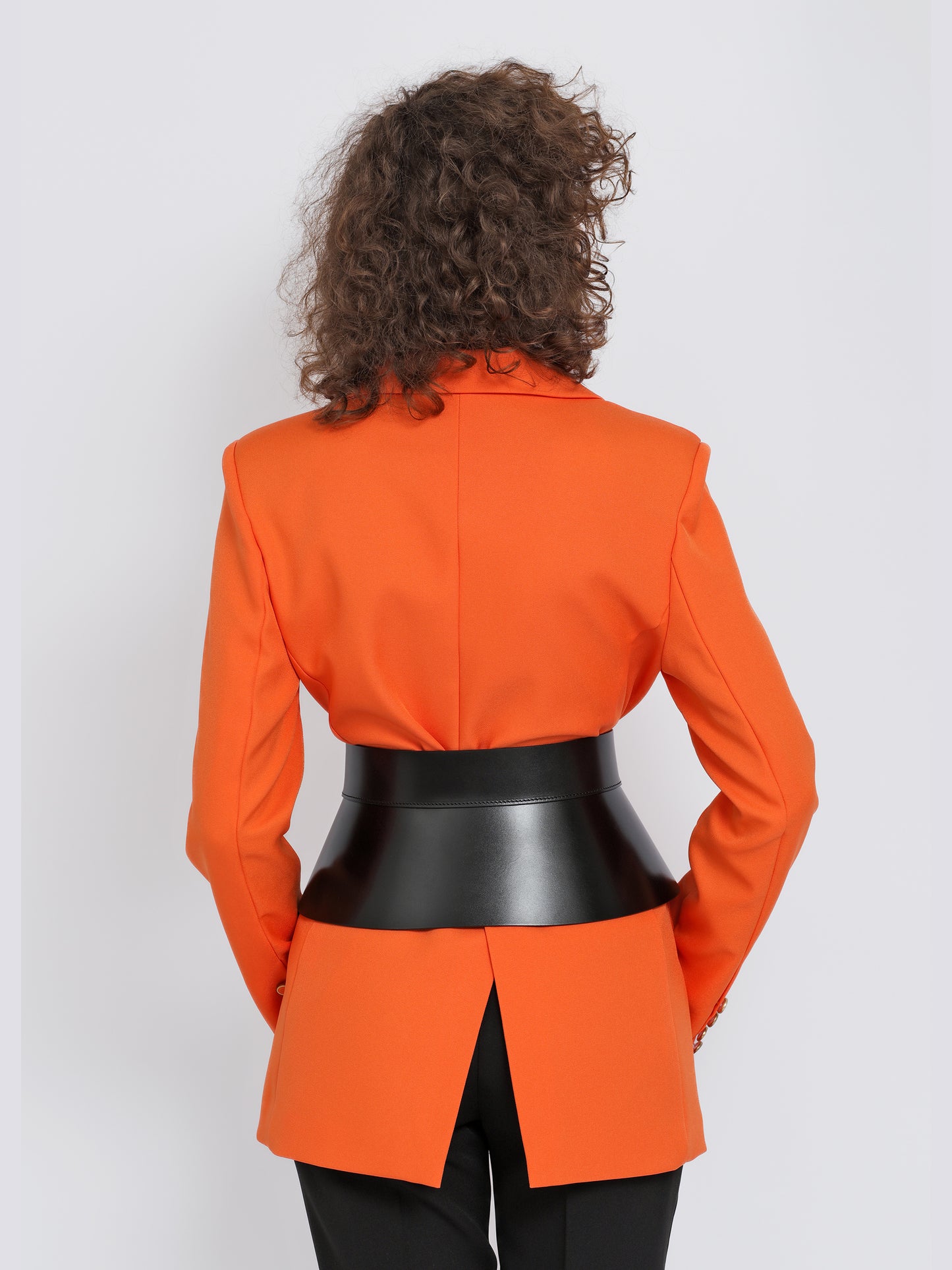 Back view of black leather peplum belt being worn over orange blazer.