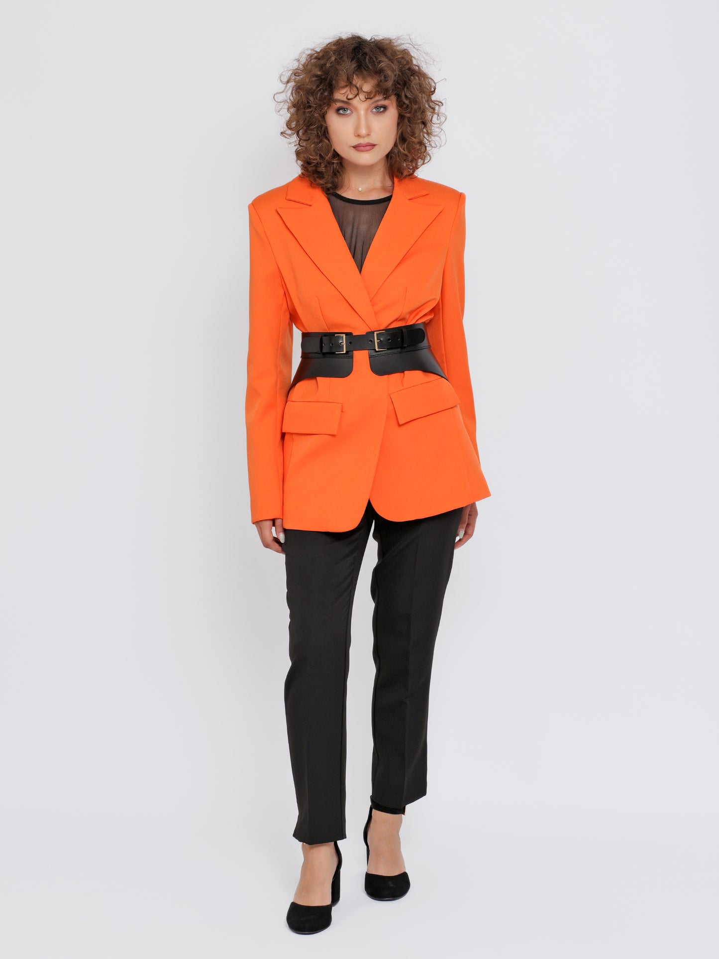 Full outfit view of peplum corset belt being worn over orange blazer and black trousers.