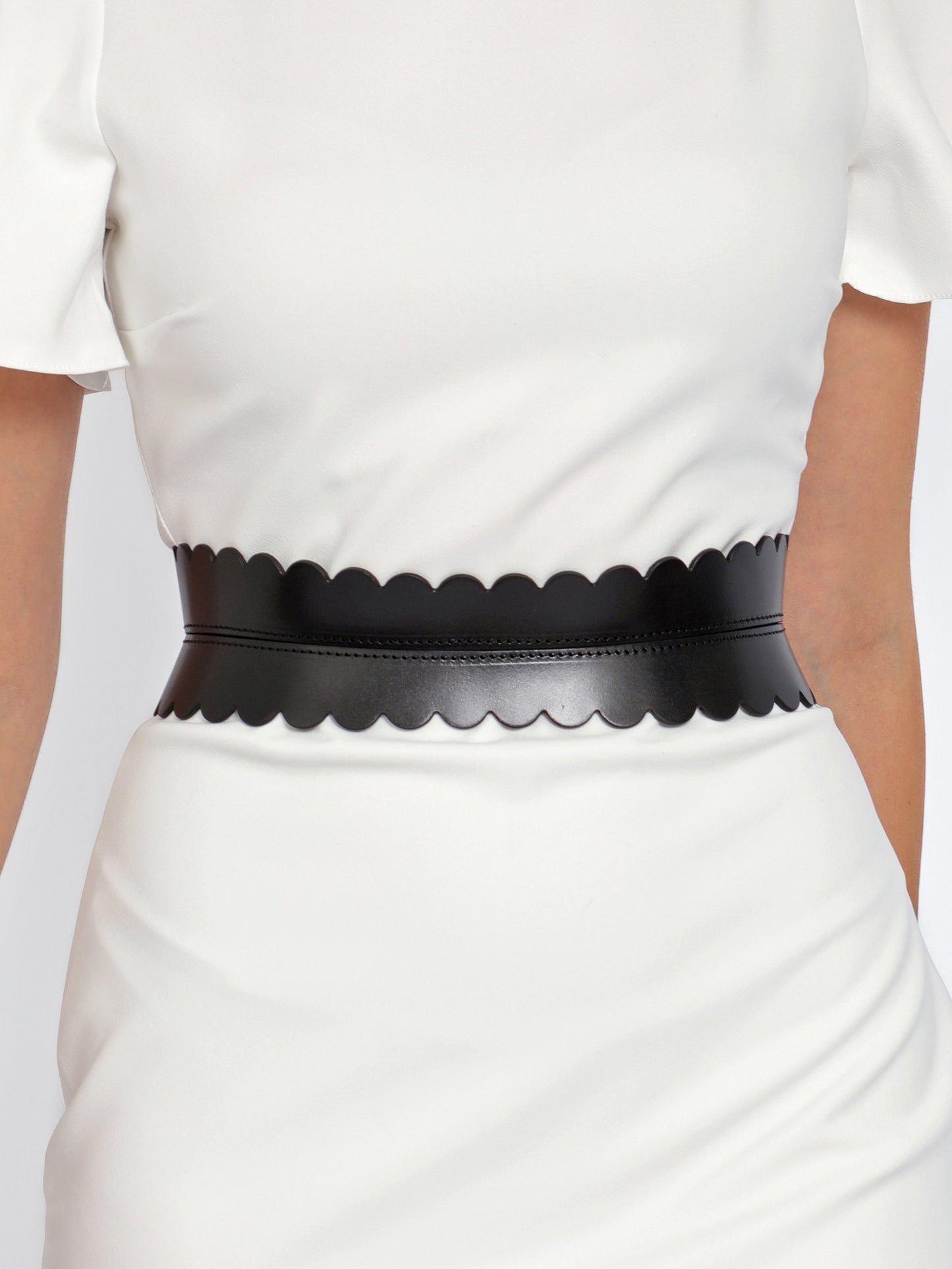 Close view of black hourglass belt being worn over white dress.