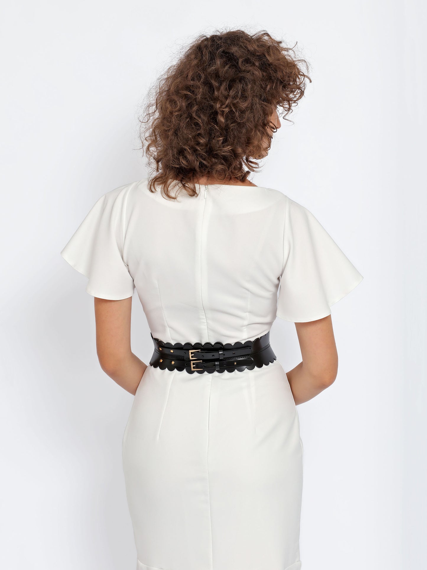 Back view of black scalloped hourglass belt being worn over white dress.