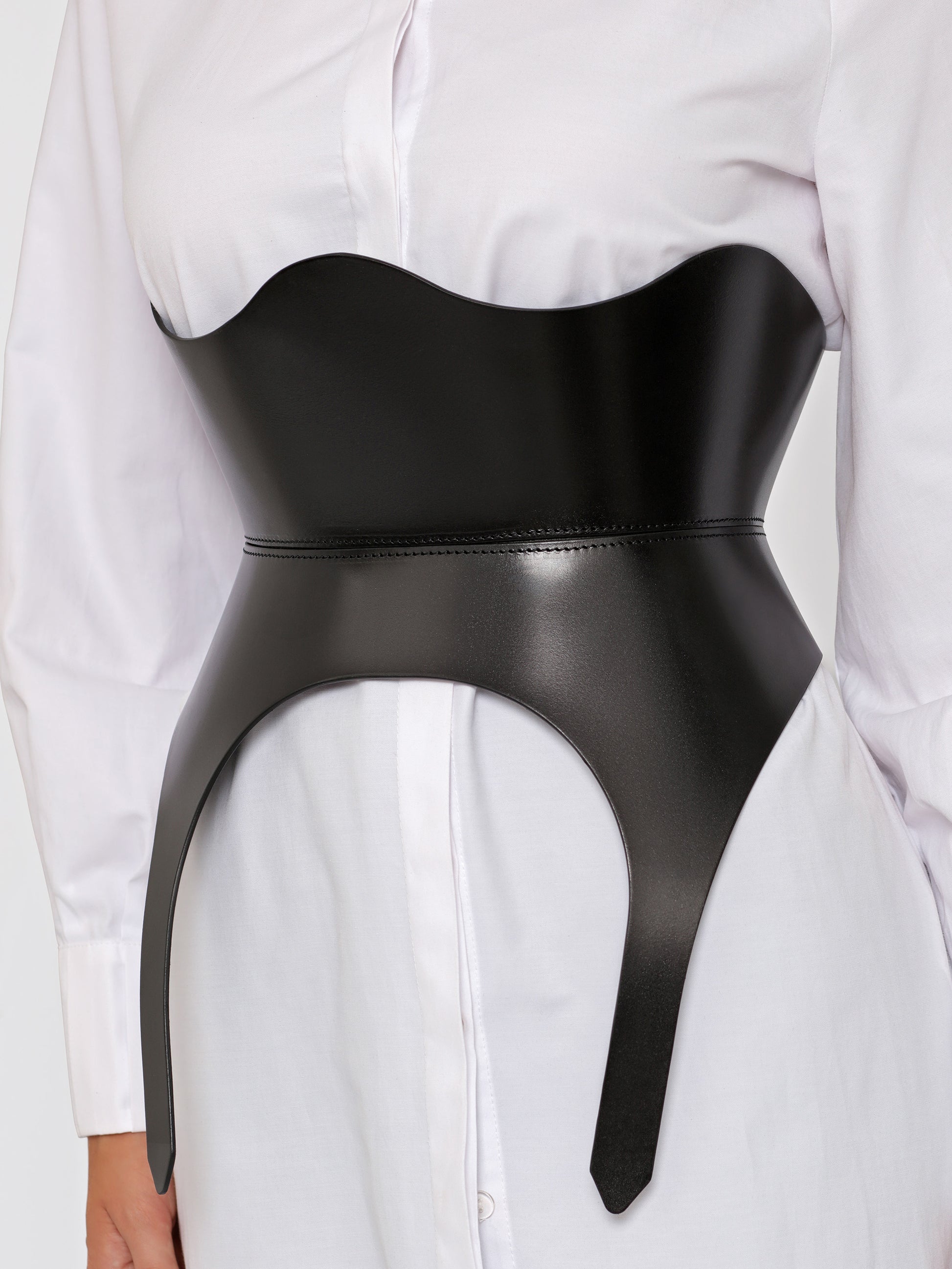 Close up view of black leather corset worn by model over white shirt.