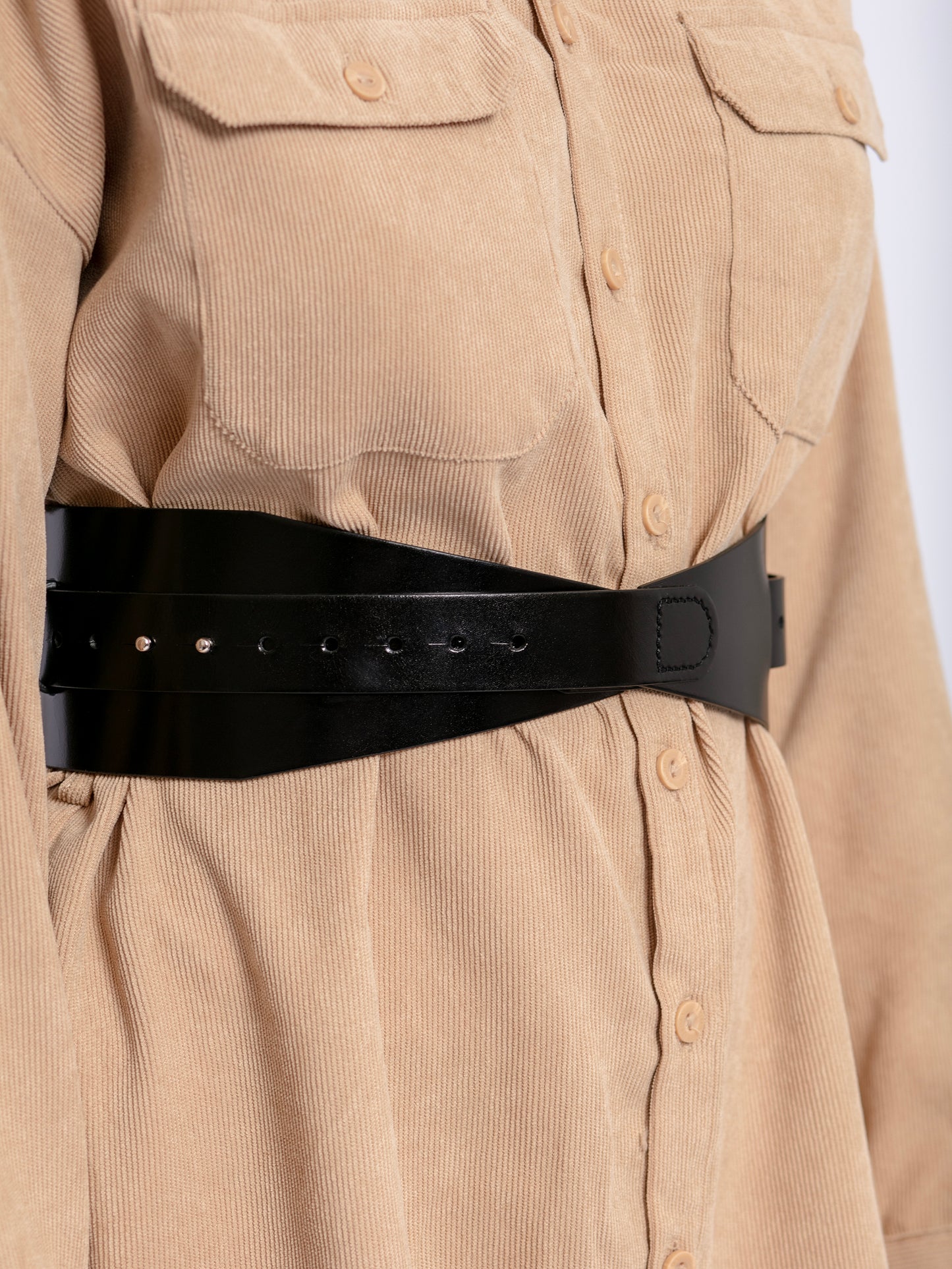 Close view of black leather corset belt worn by model over beige shirt.