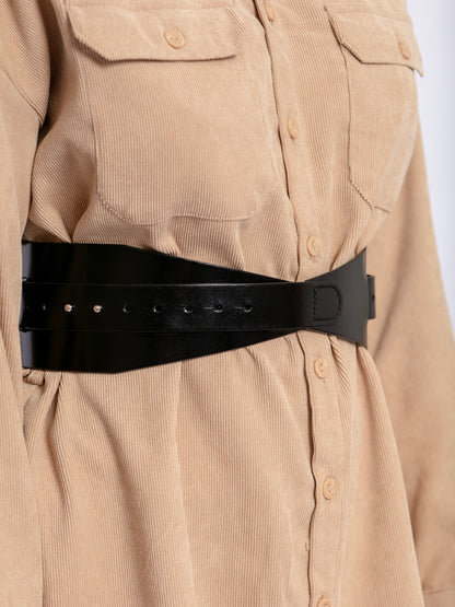 Close view of black leather corset belt worn by model over beige shirt.