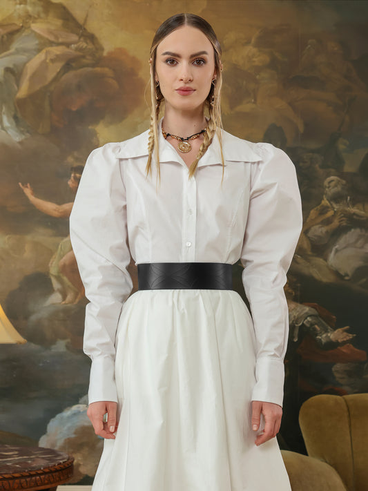 Woman wearing a white shirt dress styled with a wide black leather waist belt.