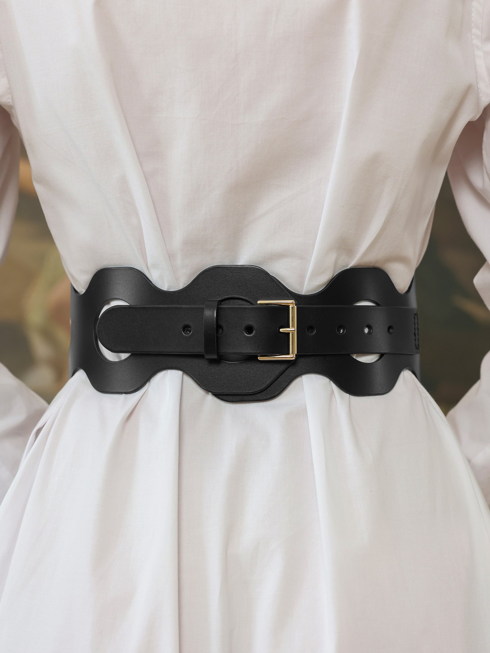 Black leather belt with large circular cutouts cinching the waist of a white dress.
