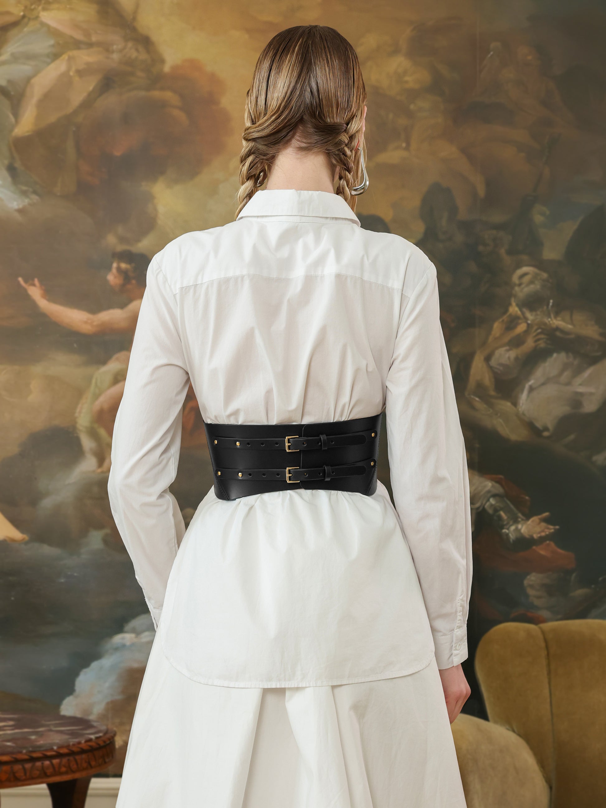 Back view of a wide black leather corset belt with double buckle fastening, adding structure to a white shirt dress.