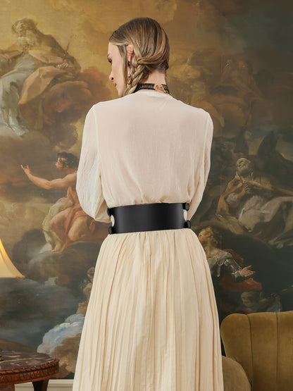 Woman in a beige dress with a black belt standing in front of an artistic mural.